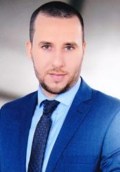 محمد جلال محمد الخالع مرتدياً بدلةً و ربطة عنق زرقاء. 