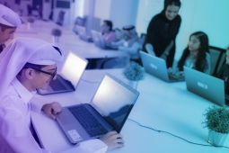  طلاب يجلسون على طاولة حيث يستخدم كل طالب جهاز كمبيوتر محمول.