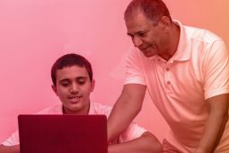 أب يساعد ابنه في القيام  بشيء ما على جهاز الكمبيوتر المحمول.