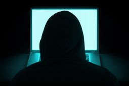 A photo showing the back of a man wearing a hoodie because he is representing the hacker and in front of him is a laptop.